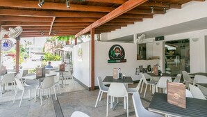 An outdoor cafe with white plastic chairs and tables, a wooden ceiling, and a sign for a restaurant. - Magic Cortesea luxury beach (Punta Cana)