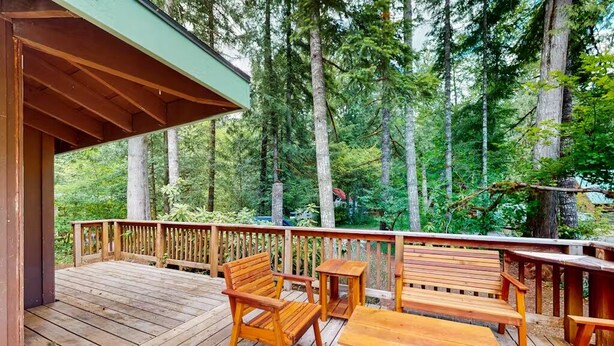 Une terrasse en bois, agréée de mobilier d’extérieur, entourée de grands arbres.