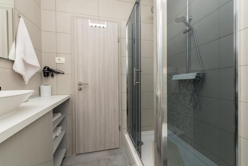 A bathroom with a white sink, a towel hanging on the wall, a shower with a glass door, and a wooden door.