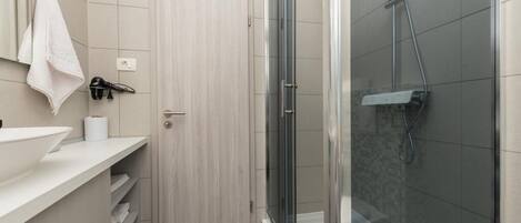 A bathroom with a white sink, a towel hanging on the wall, a shower with a glass door, and a wooden door.