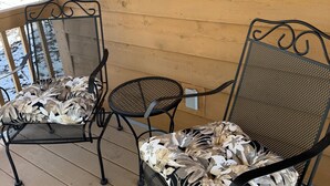 A wooden deck with two metal chairs and a small round table.