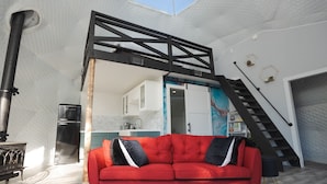 Un salon moderne avec un canapé rouge, un escalier noir et une cuisine en arrière-plan.