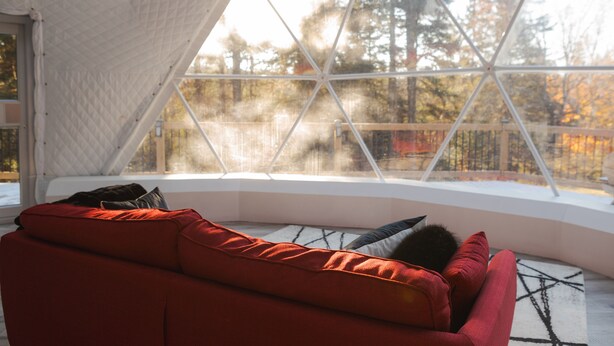 Une pièce chaleureuse avec un canapé rouge, un tapis à motifs et une grande fenêtre donnant sur les arbres.