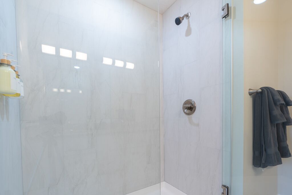 Ein modernes Badezimmer mit Duschkabine aus Glas, einem sichtbaren Handtuchhalter und einer Shampooflasche an der Wand.