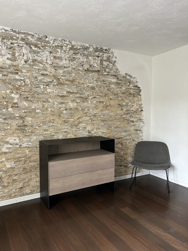 Een kamer met een stenen muur, een houten kast en een grijze stoel.
