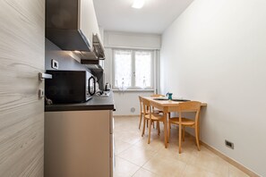 A compact kitchen with a microwave, stove, and a small dining table with chairs. - Mare Celeste (Arma di Taggia)