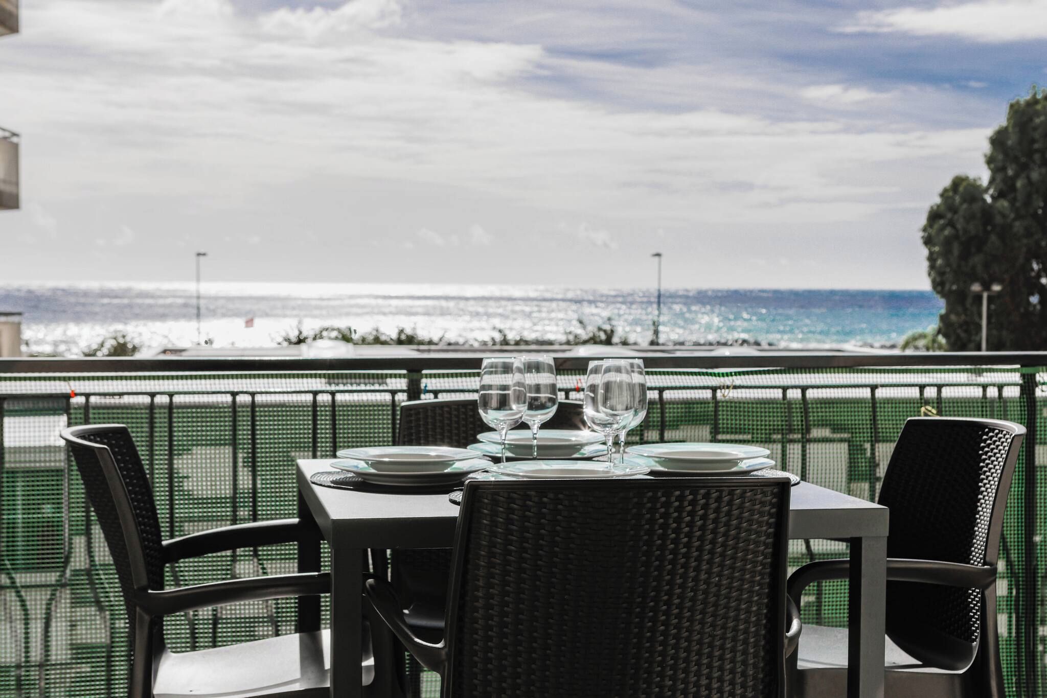 An outdoor dining area with a view of the ocean, featuring a table set with plates and glasses.
