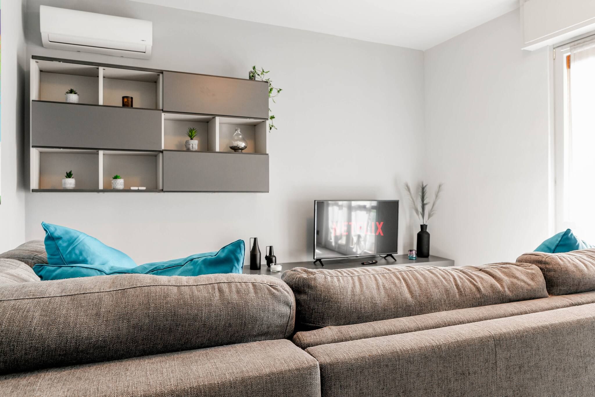 A modern living room with a grey sectional sofa, a flat-screen TV, and built-in shelving with decorative items.