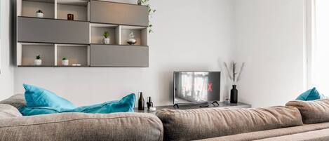 A modern living room with a grey sectional sofa, a flat-screen TV, and built-in shelving with decorative items.