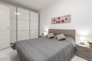 Ein Schlafzimmer mit Bett, Nachttisch, Lampe, Wandbild und Kleiderschrank.
