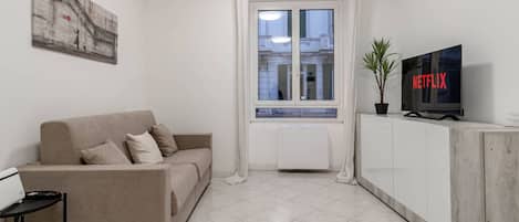 A modern living room with a beige sofa, a flat-screen TV, and a potted plant.