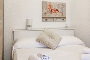 A neatly made bed with a single pillow and a folded towel, a wall-mounted lamp, and a decorative painting above the bed. - M OLD TOWN - Sanremo - Casinò (Sanremo)