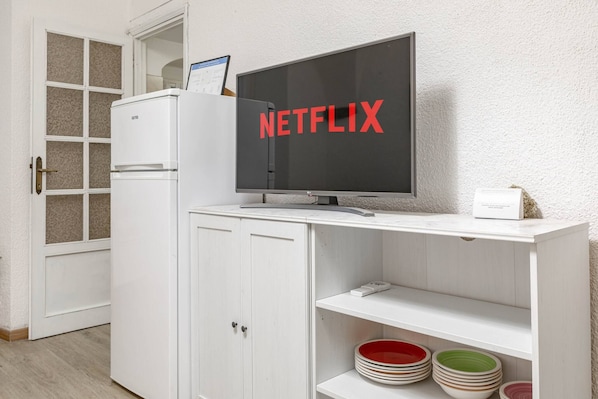 A white entertainment unit with a flat-screen TV displaying 'NETFLIX' in red letters, a small white box, and a stack of plates on shelves. - M OLD TOWN - Sanremo - Casinò (Sanremo)