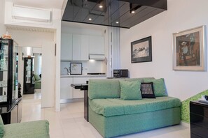 Een moderne woonkamer met een groene bank, een eethoek en een keuken op de achtergrond, met een lijstwerkfoto aan de muur.