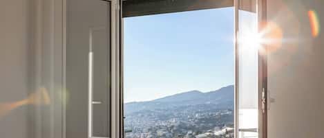 A room with a large window offering a view of a cityscape and mountains.