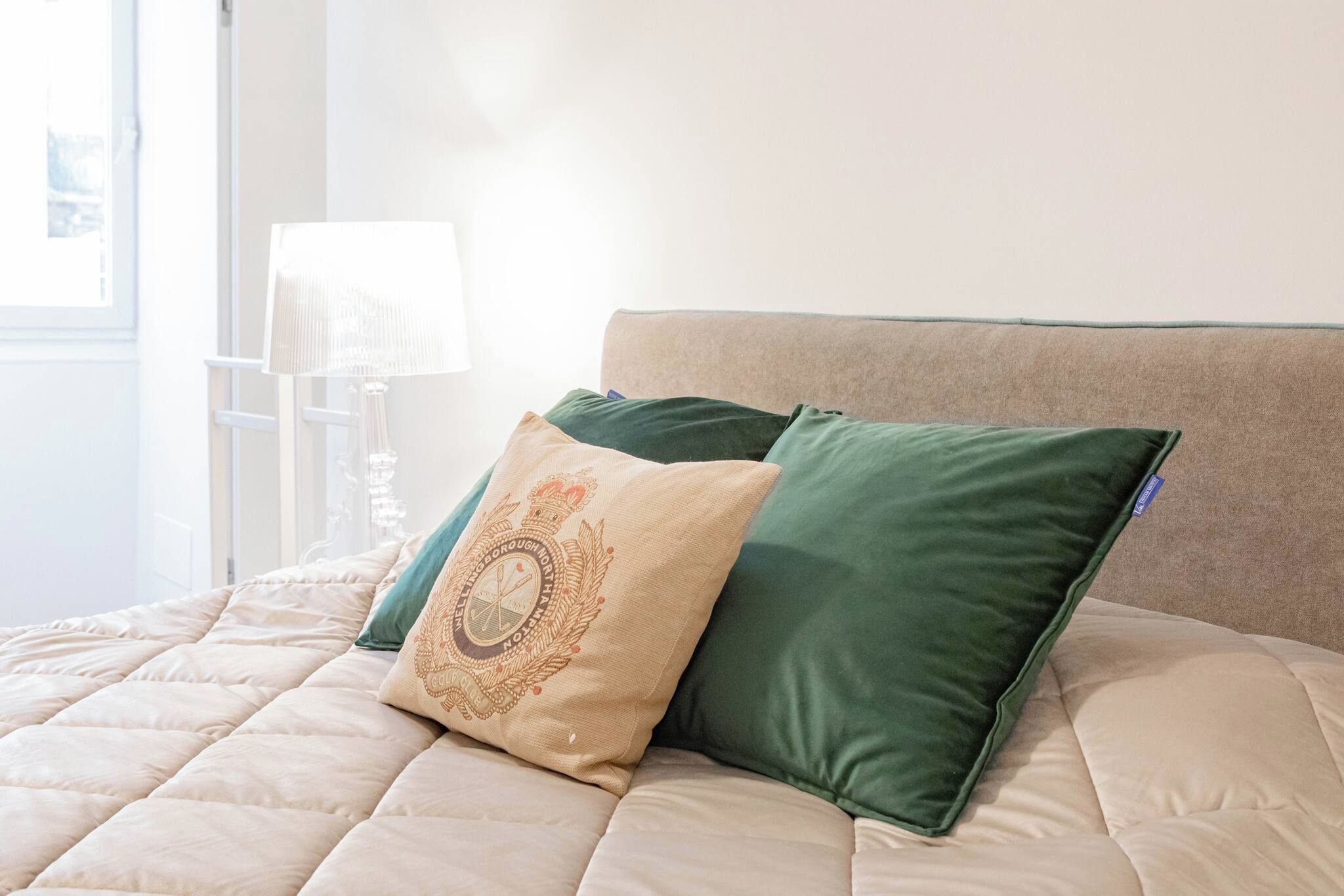 A bed with a quilted headboard, two pillows, and a bedside lamp.