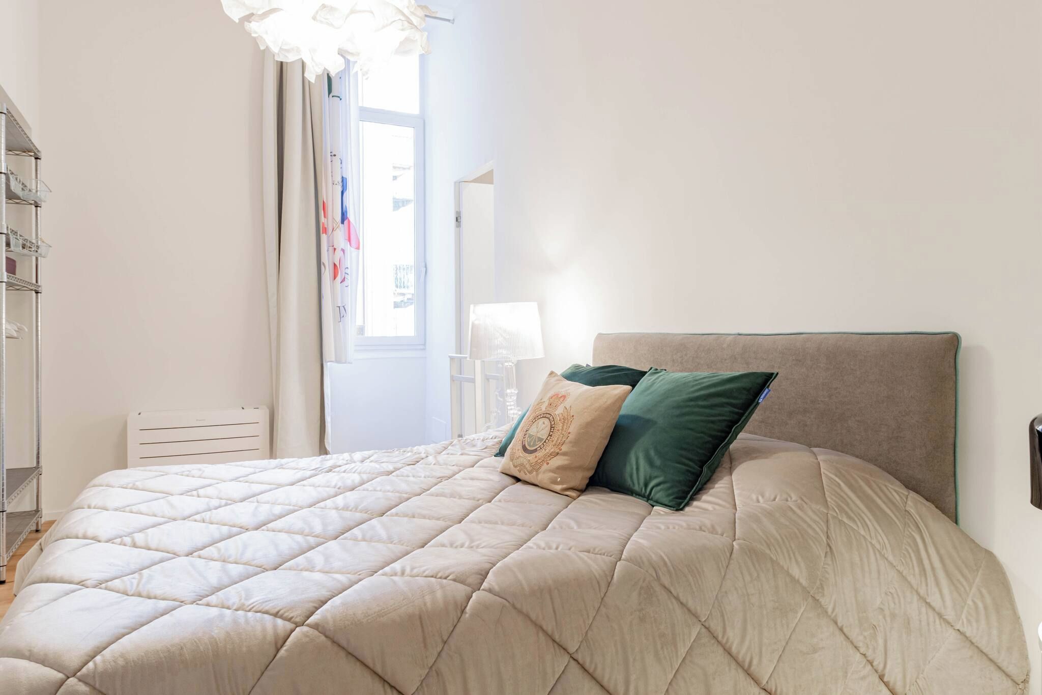 Un dormitorio con cama, cortinas en la ventana, una mesita de noche y una lámpara.