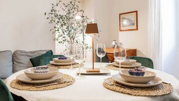 A dining table set with plates, bowls, and wine glasses, surrounded by chairs and a plant.