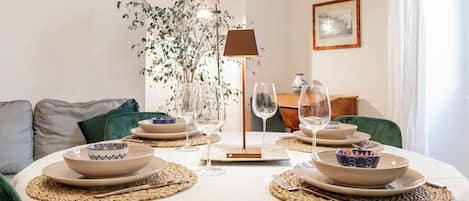A dining table set with plates, bowls, and wine glasses, surrounded by chairs and a plant.