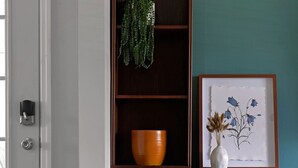 A wooden console table with a vase and a framed picture against a teal wall, a bowl on the lower shelf, and a door with a handle and lock. - WELCOME TO THE OWL'S NEST - 2 BEDROOM HOME IN AUGUSTA, WINERIES & THE KATY TRAIL (Augusta)