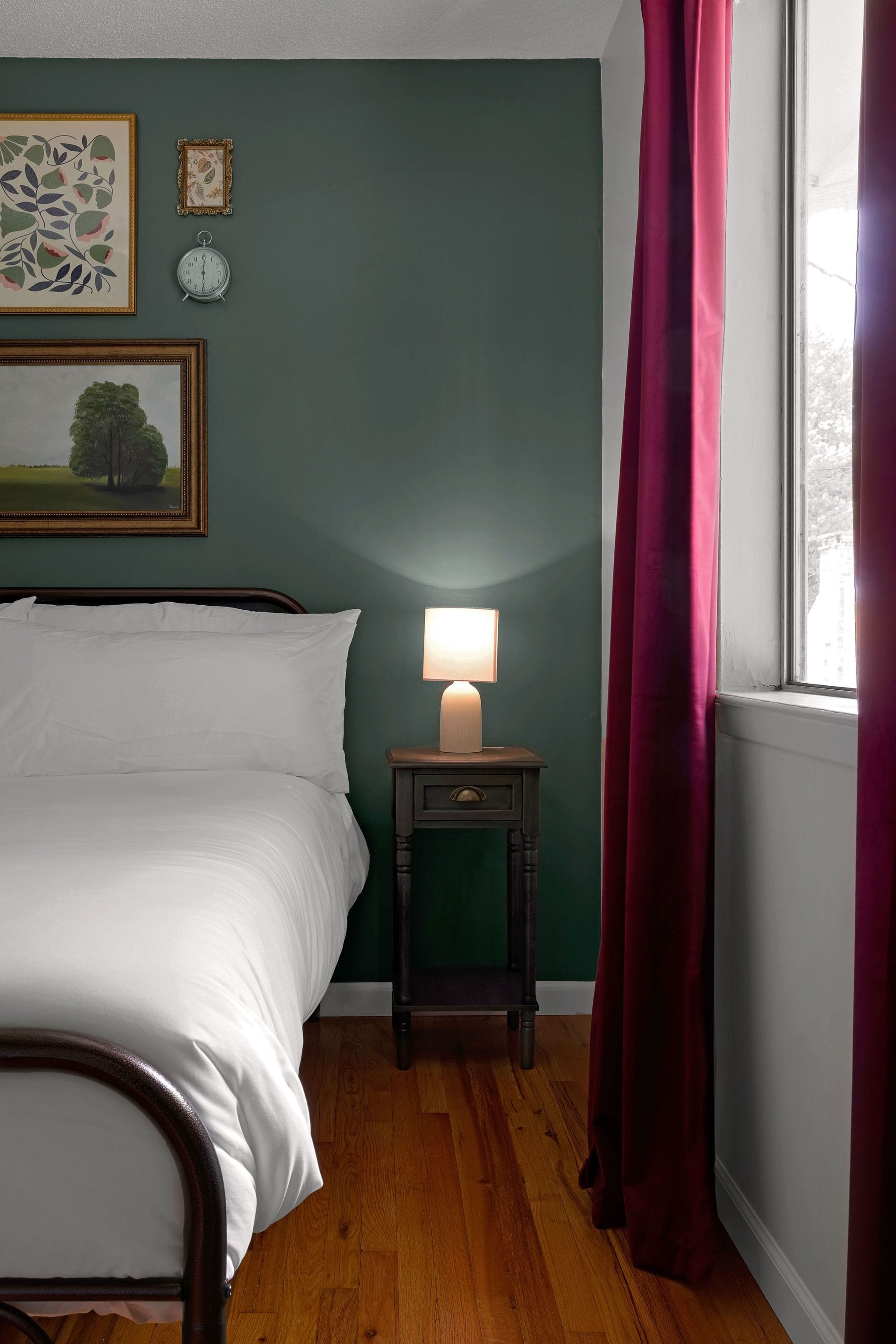 Een slaapkamer met een bed, een nachtkastje met een lamp, een klok en lijstwerken aan de muur.