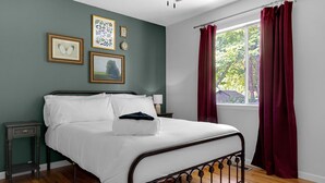 A neatly made bed with white linens, a bedside table with a lamp, and a window with red curtains. - WELCOME TO THE OWL'S NEST - 2 BEDROOM HOME IN AUGUSTA, WINERIES & THE KATY TRAIL (Augusta)