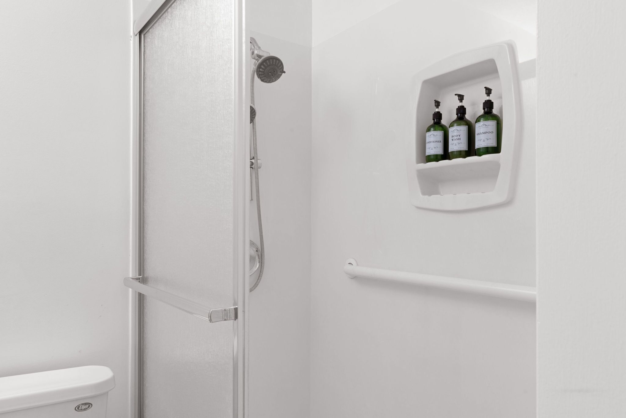 Une salle de bain équipée d’une douche, de toilettes et d’une étagère sur laquelle se trouvent trois bouteilles de shampoing et d’après-shampoing.