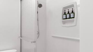 Une salle de bain équipée d’une douche, de toilettes et d’une étagère sur laquelle se trouvent trois bouteilles de shampoing et d’après-shampoing.