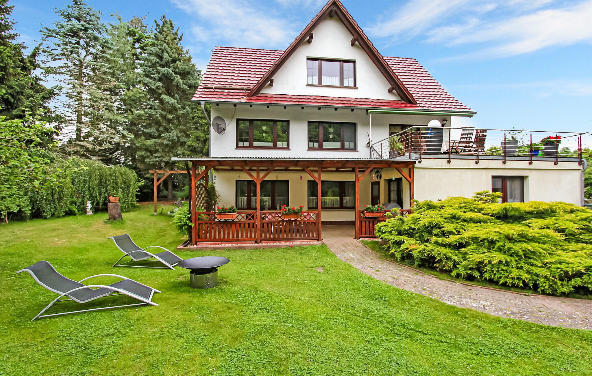 Ein zweistöckiges Haus mit rotem Ziegeldach, einem Balkon mit Gartenmöbeln und einem gepflegten Garten mit Rasen und Sträuchern.