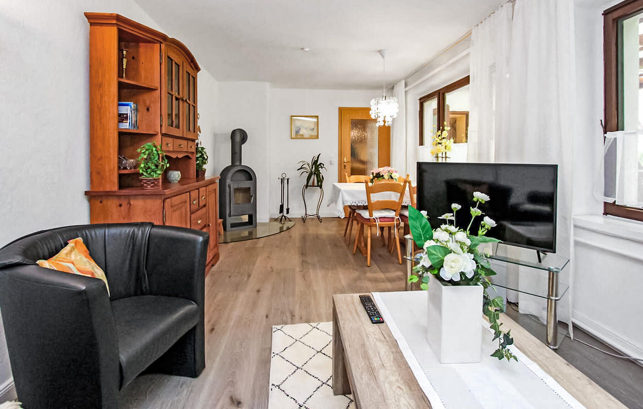 Una sala de estar con un sofá de cuero negro, un aparador de madera, una chimenea, una zona de comedor con mesa y sillas, y un televisor sobre un mueble.