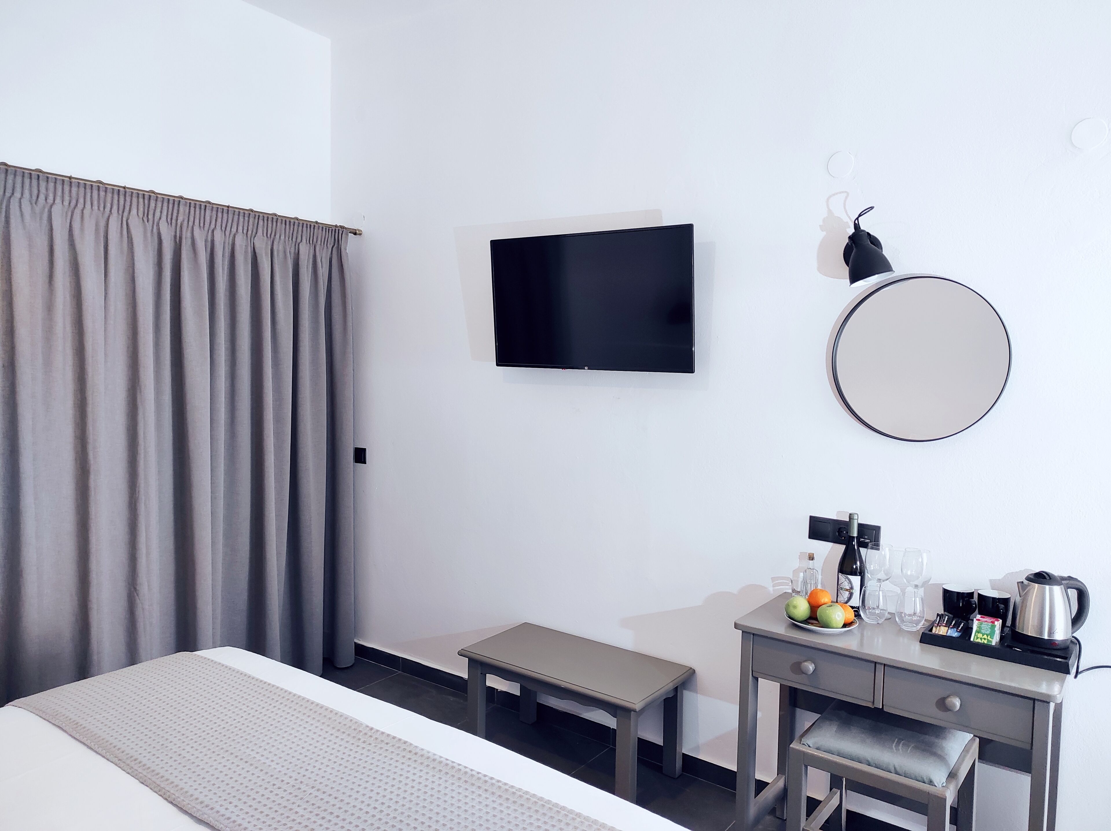 A hotel room with a bed, a desk with a kettle, a coffee maker, and a fruit bowl.