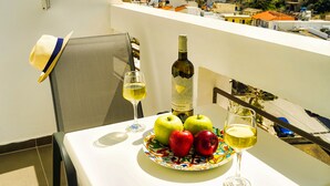 Een balkon met een tafel gedekt voor twee personen, met een fles wijn, twee glazen en een bord met appels en een hoed.