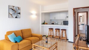 A living room with a sofa, a coffee table, and a kitchen area with stools. - Villa Blanca, Fkk-apartment Nr. 2 in Charco del Palo mit Schwimmbad, Meernähe (Charco del Palo)