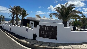 A sign for Villa Blanca with a clear view of the ocean and palm trees in the background. - Villa Blanca, Fkk-apartment Nr. 2 in Charco del Palo mit Schwimmbad, Meernähe (Charco del Palo)