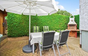 Eine Terrasse im Freien mit Tisch für vier Personen, umgeben von Stühlen, unter einem weißen Sonnenschirm.