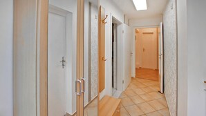 Un couloir avec des portes blanches, certaines dotées de poignées et d’autres de serrures. Un banc se trouve au milieu du couloir.