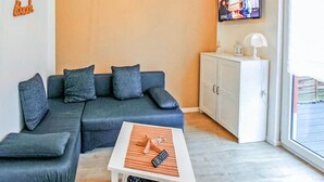 A living room with a sectional sofa, a small table with a remote control, a cabinet, and a television mounted on the wall. - Ferienhaus Zinnowitz (Seebad) (Zinnowitz (Seebad))