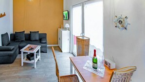 A modern living room with a grey sofa, a small white table, and a wicker chair. There is a bottle of wine and a glass on the table. - Ferienhaus Zinnowitz (Seebad) (Zinnowitz (Seebad))