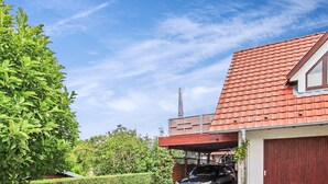 Um edifício residencial com telhado de telhas vermelhas, chaminé e garagem com um carro estacionado dentro.