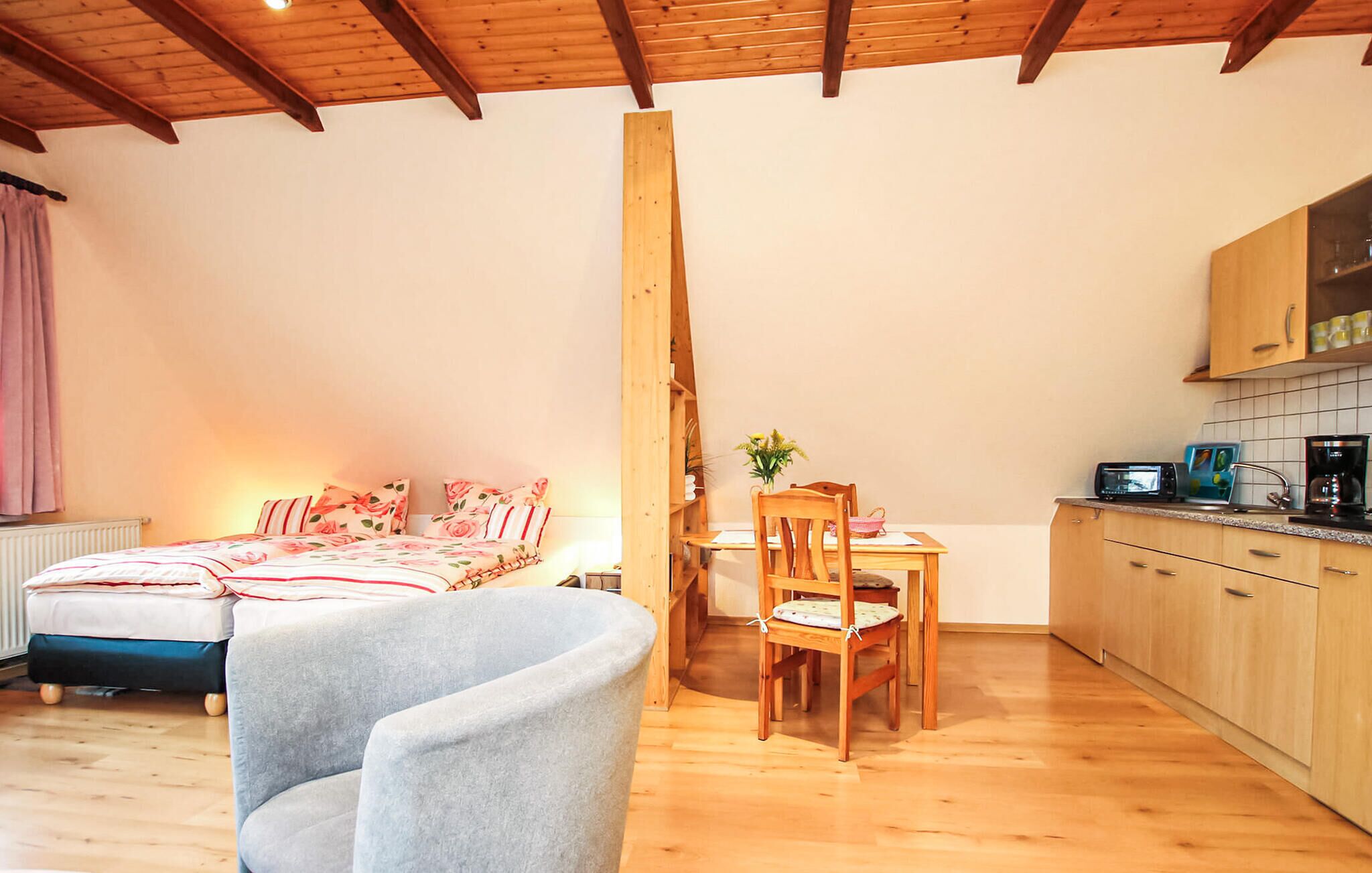 A cozy room with a bed, a dining table with chairs, a kitchen area, and a wooden ceiling.