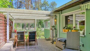 Ein überdachter Patio-Bereich mit Tisch und Stühlen, ein kleiner Tisch mit Dekoration und ein Korbstuhl.