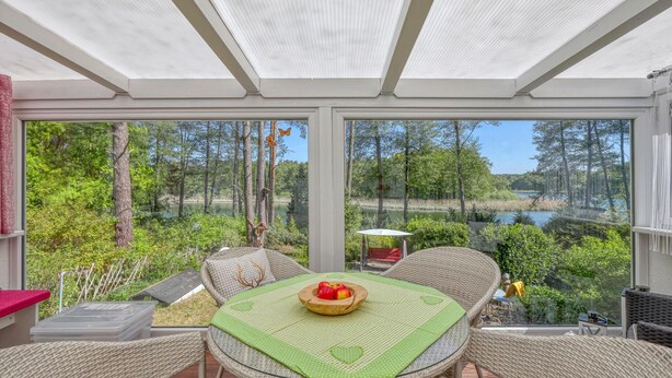 Eine überdachte Terrasse mit Korbmöbeln, einem Tisch mit herzmusterbezogener Tischdecke und einer Obstschale.