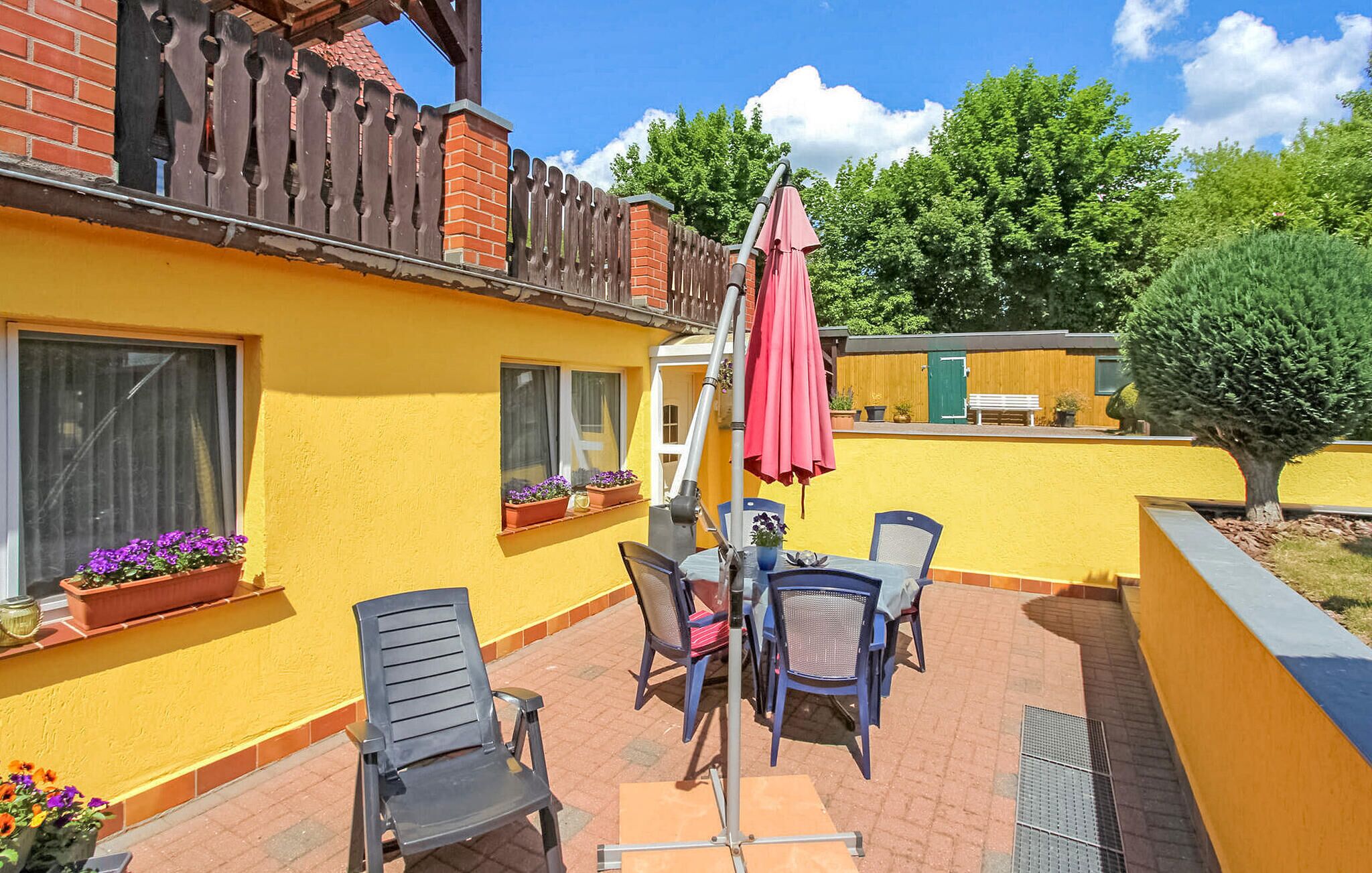 A yellow building with a patio area featuring two chairs, a table, and a red umbrella.