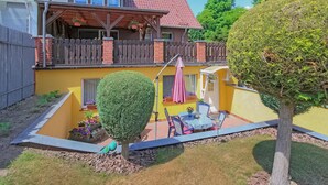 Un patio con una mesa y sillas, un pequeño árbol y un edificio amarillo de techo rojo.