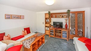 Una sala de estar con un sofá, una mesa de centro, un mueble para televisión y un aparador con puertas de cristal.