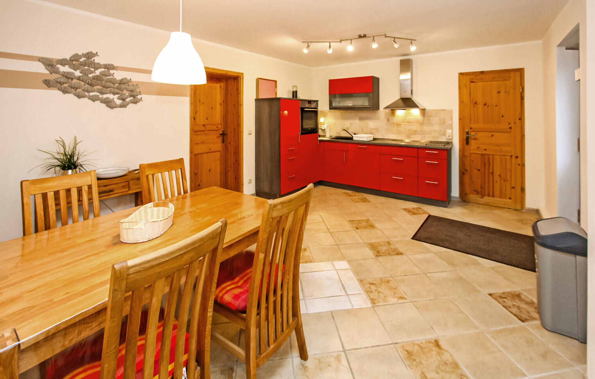 A modern kitchen with red cabinets, a wooden dining table, and a hanging light fixture.