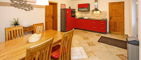 A modern kitchen with red cabinets, a wooden dining table, and a hanging light fixture.