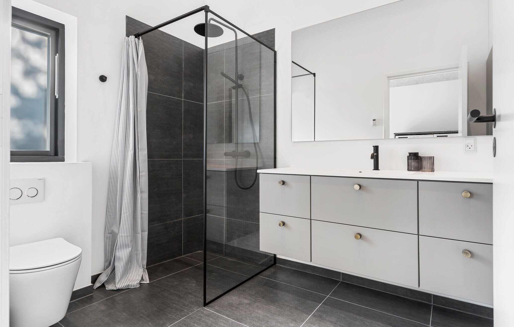 Une salle de bain moderne avec une douche à parois de verre, un meuble-lavabo blanc doté de tiroirs et un grand miroir au-dessus du lavabo.