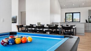 Een moderne woonkamer met een pooltafel, een eethoek en een keuken.