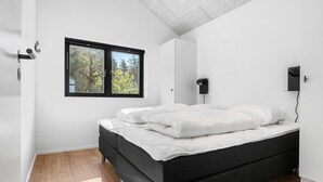 Een moderne slaapkamer met een groot bed, een raam met uitzicht op bomen, een wandlamp en een deur met een handvat.